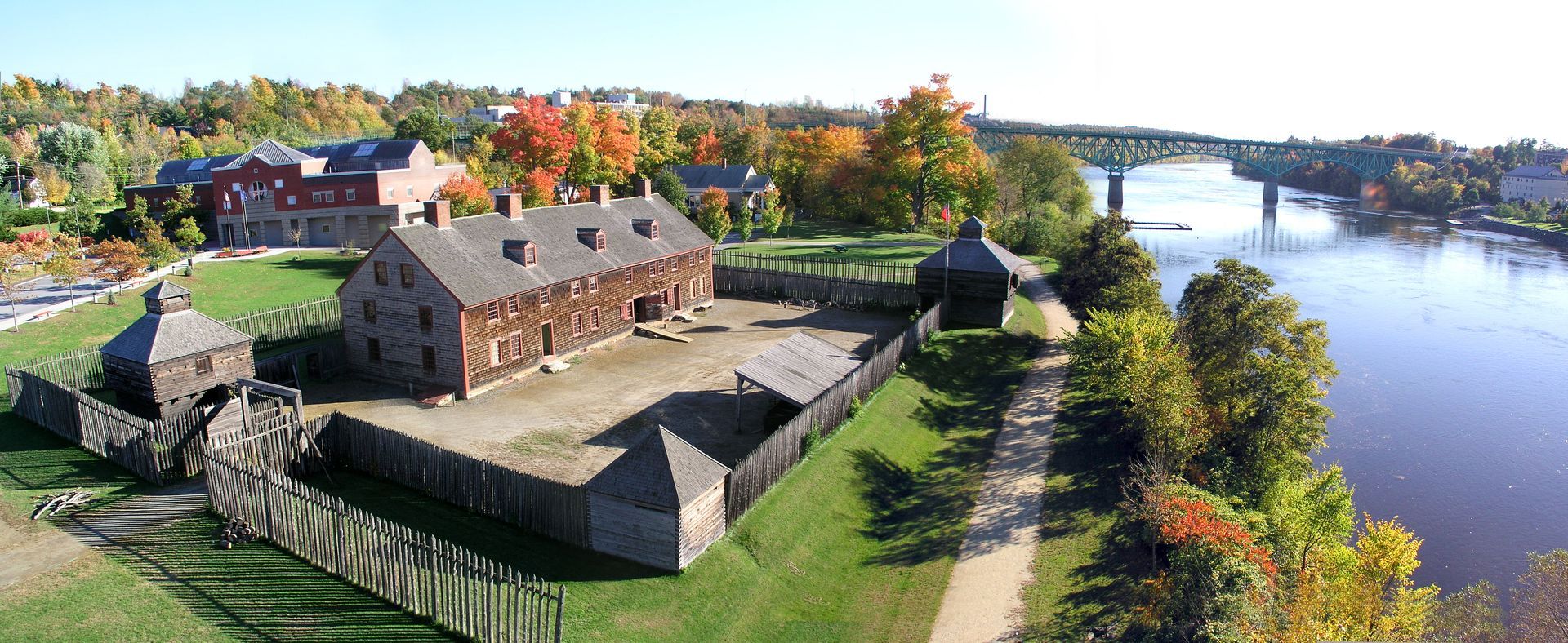 Aerial view of a historic stone fort beside a river, with autumn trees and a bridge in the distance