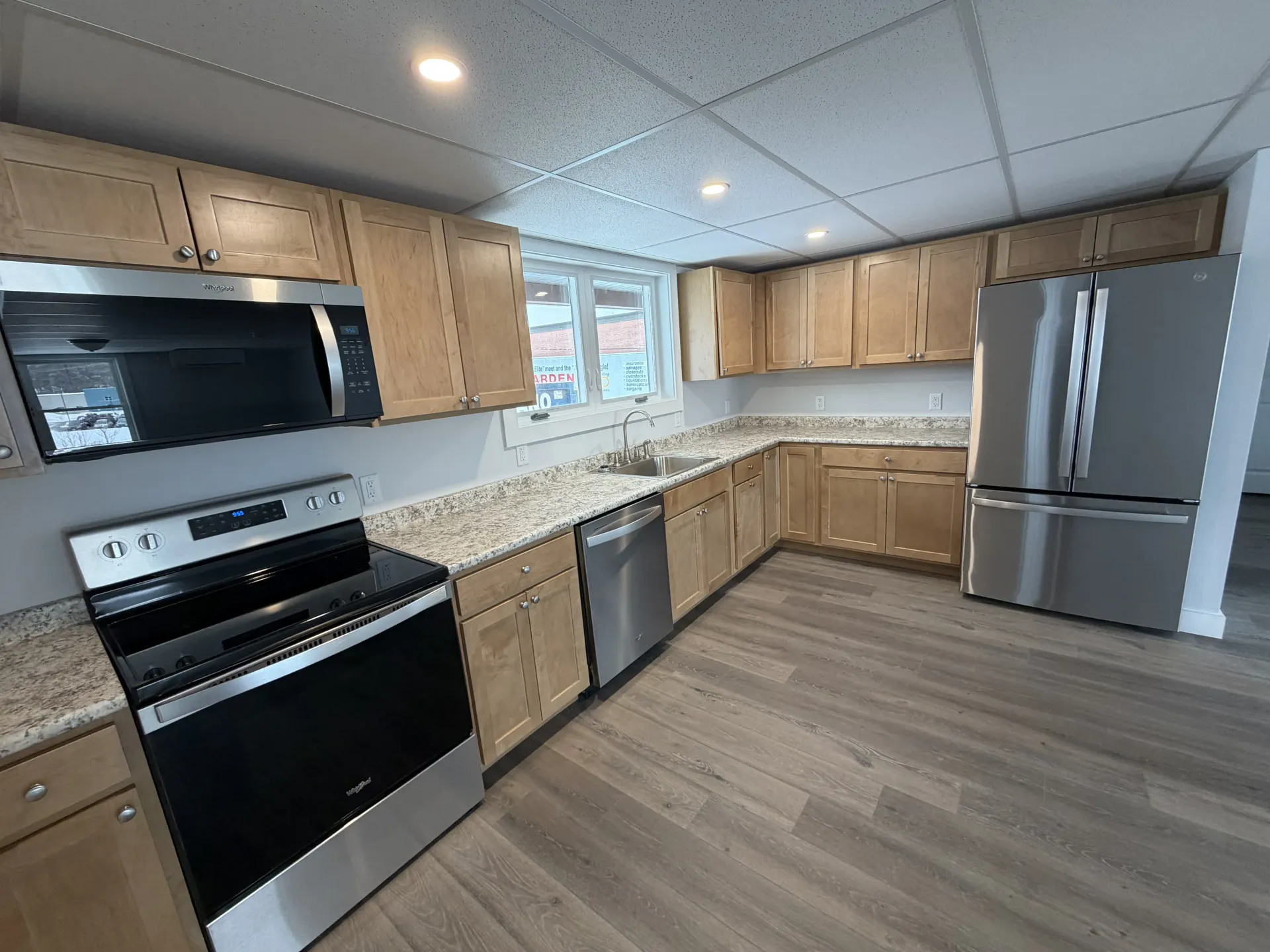 Bright modern kitchen with light wood cabinets, stainless appliances, and wood-look flooring