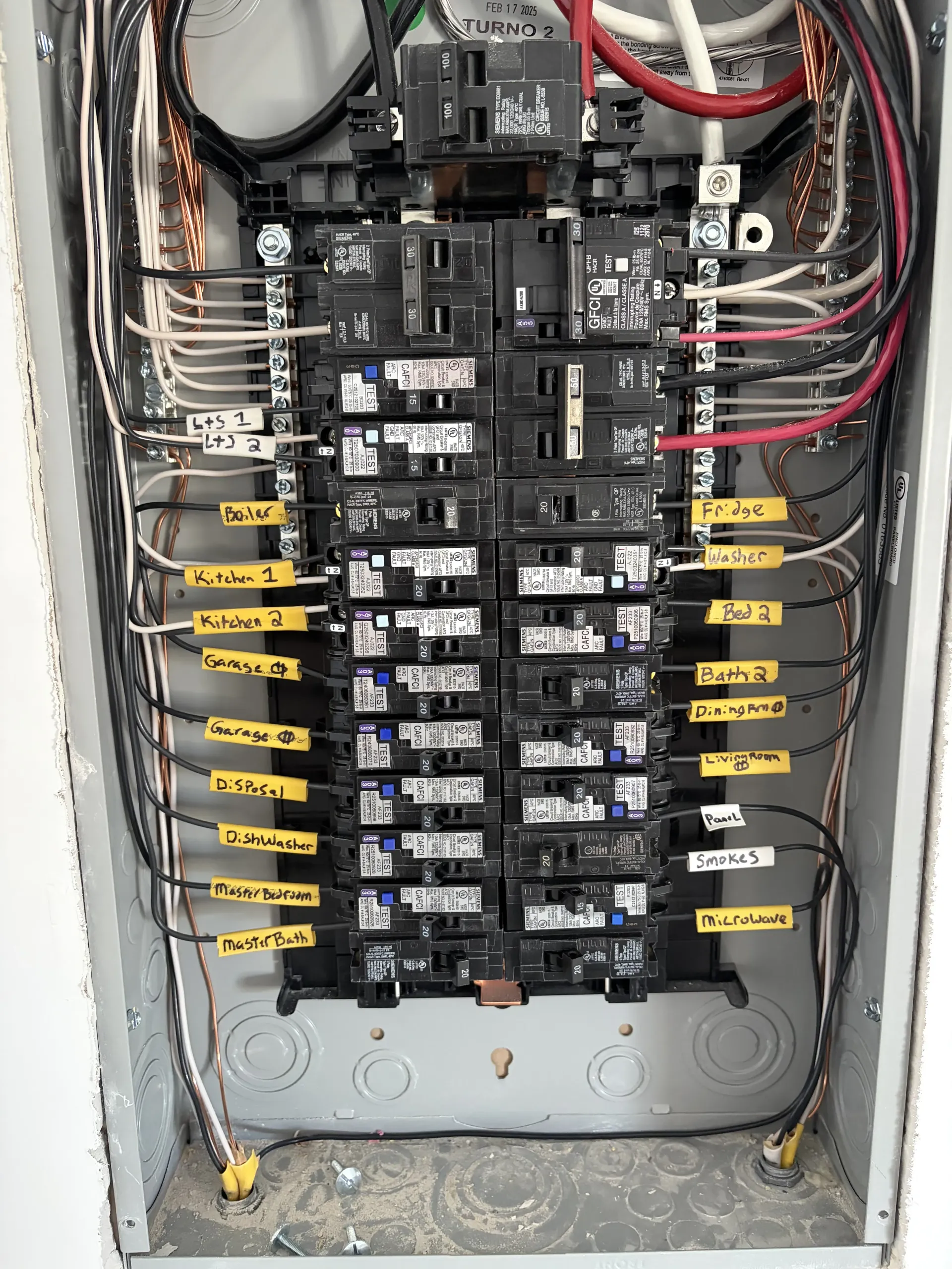 Open electrical breaker panel with rows of black switches and red wiring.