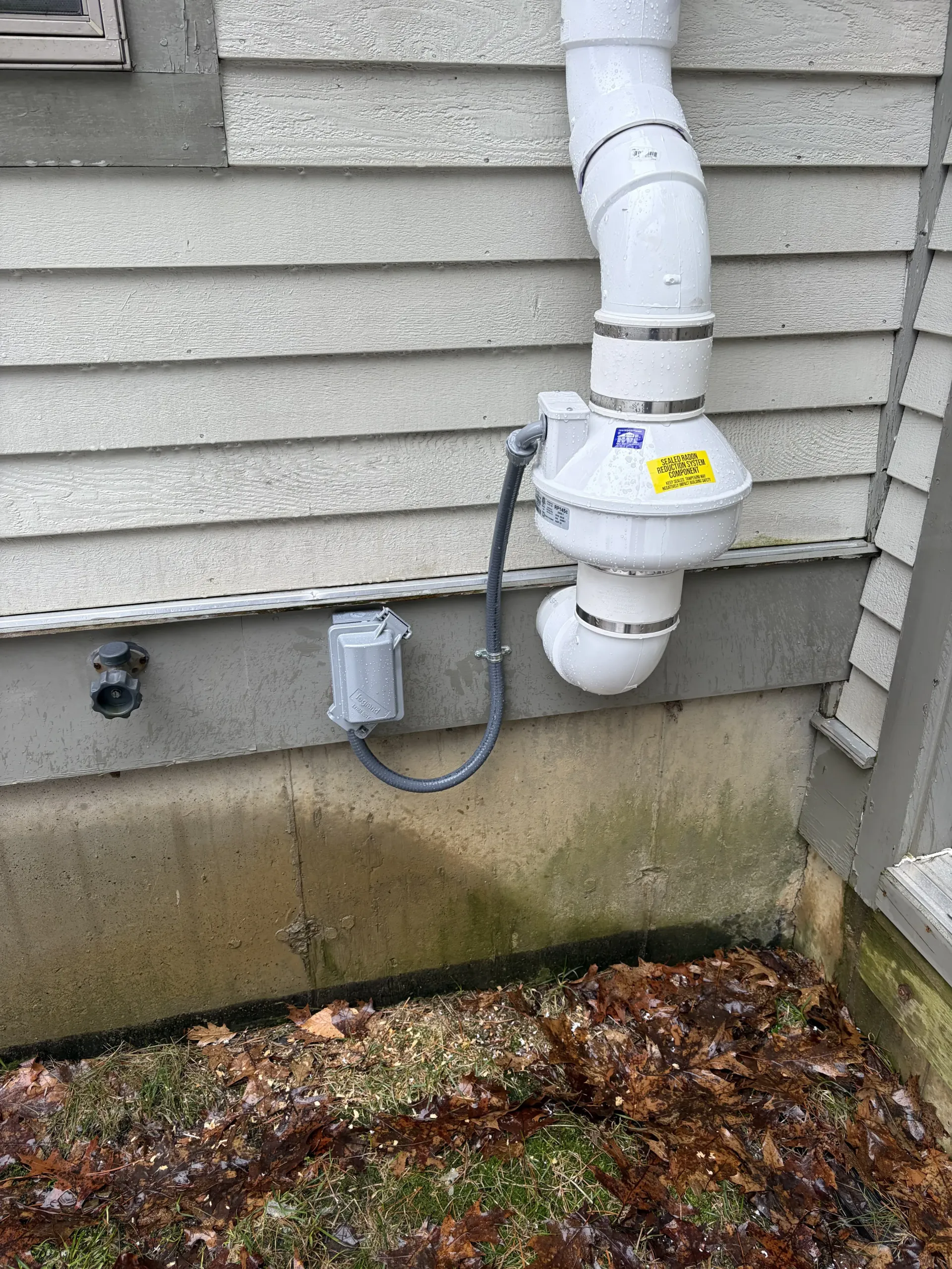 Utility meter and white PVC pipes on an exterior house wall above a concrete foundation.