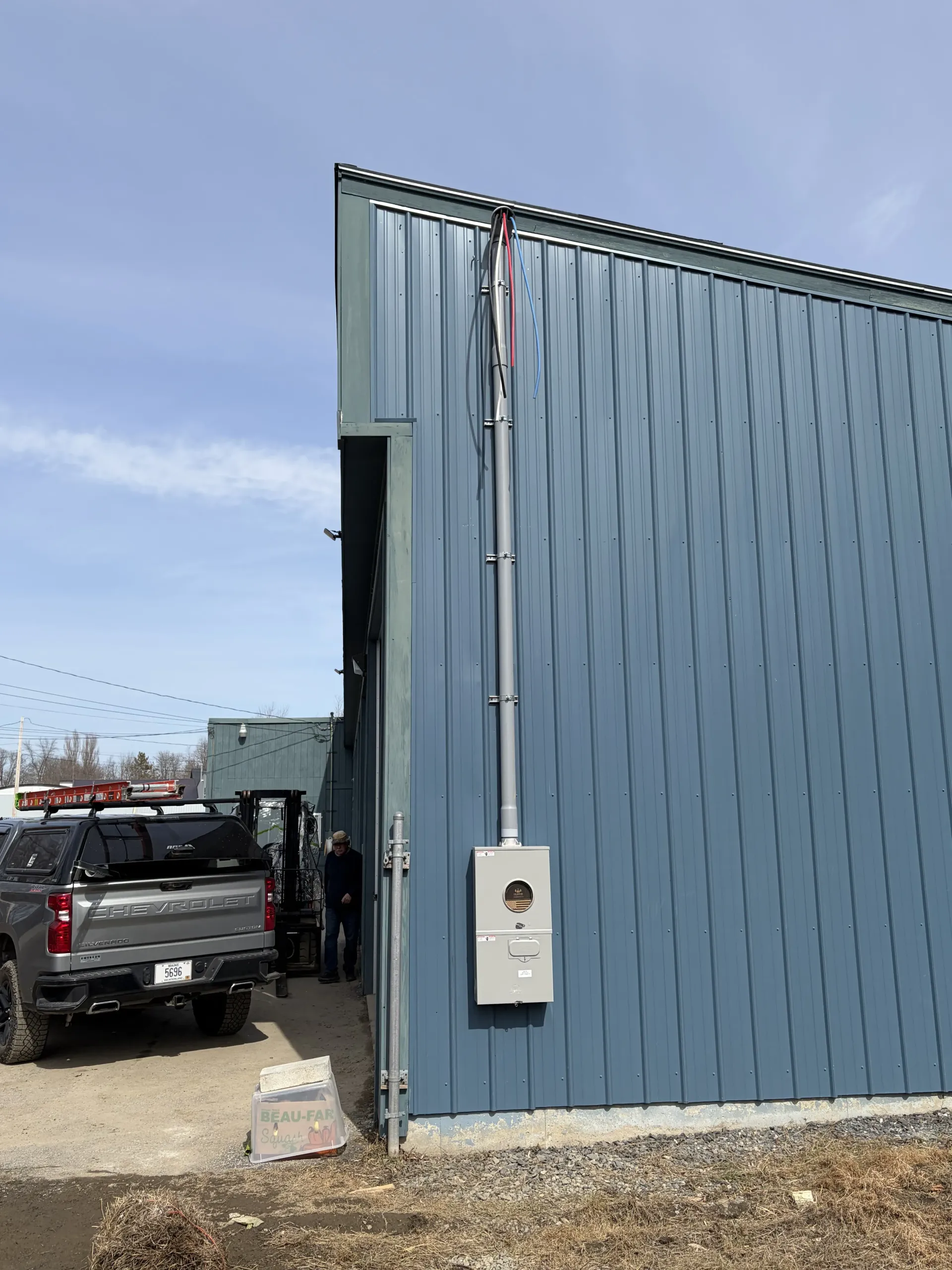 Blue metal building exterior with a parked black pickup truck beside it and a small utility box on the wall