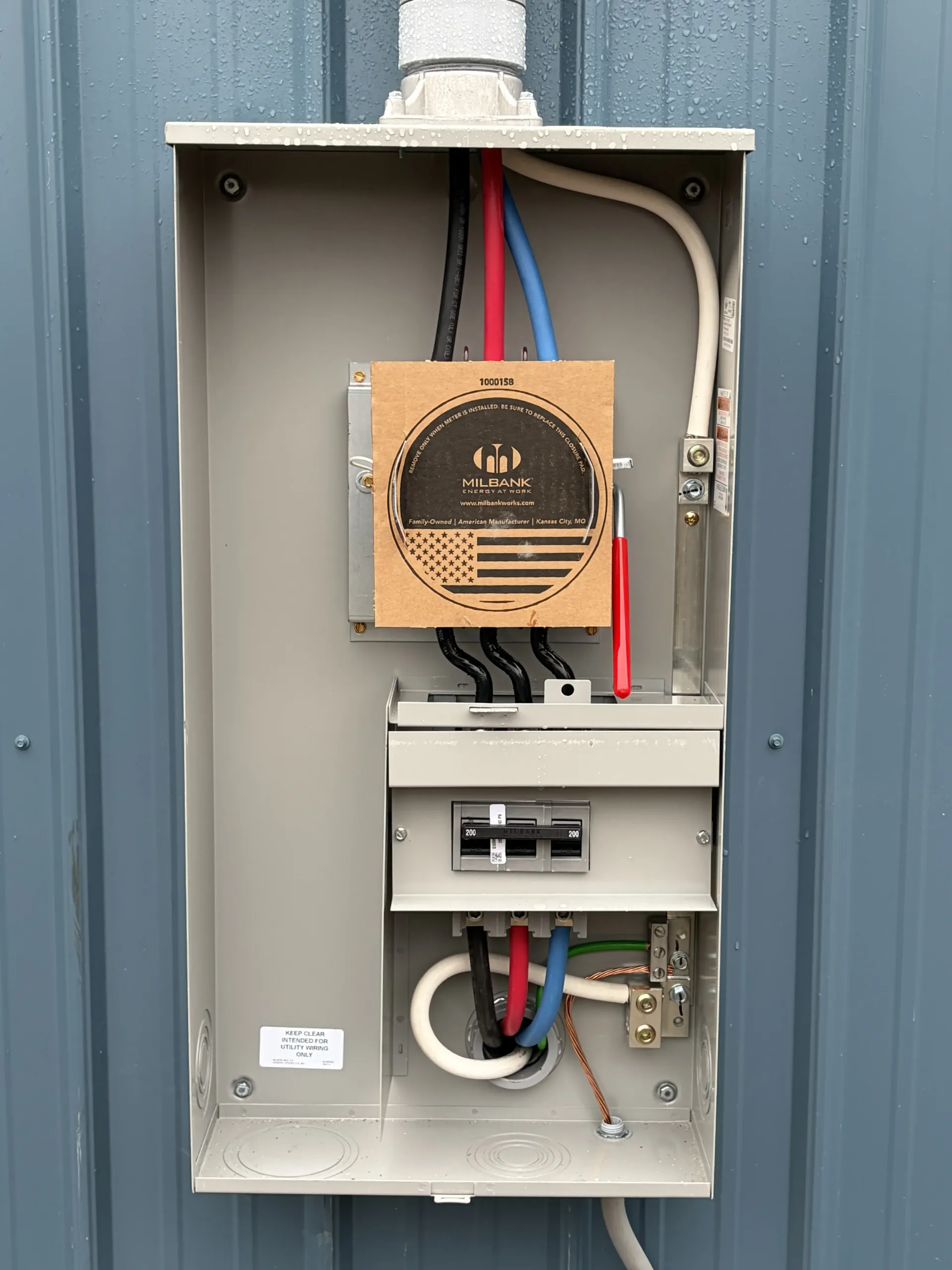 Open electrical panel with exposed red, blue, white, and black wires in a gray metal box.