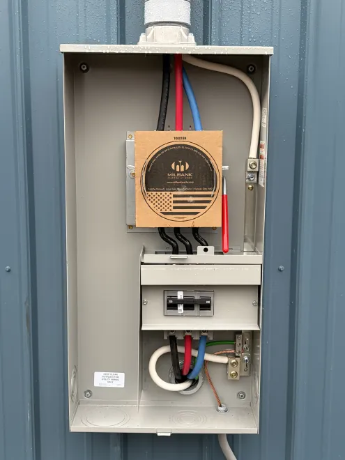 Open electrical panel with wires and meter mounted on a gray wall