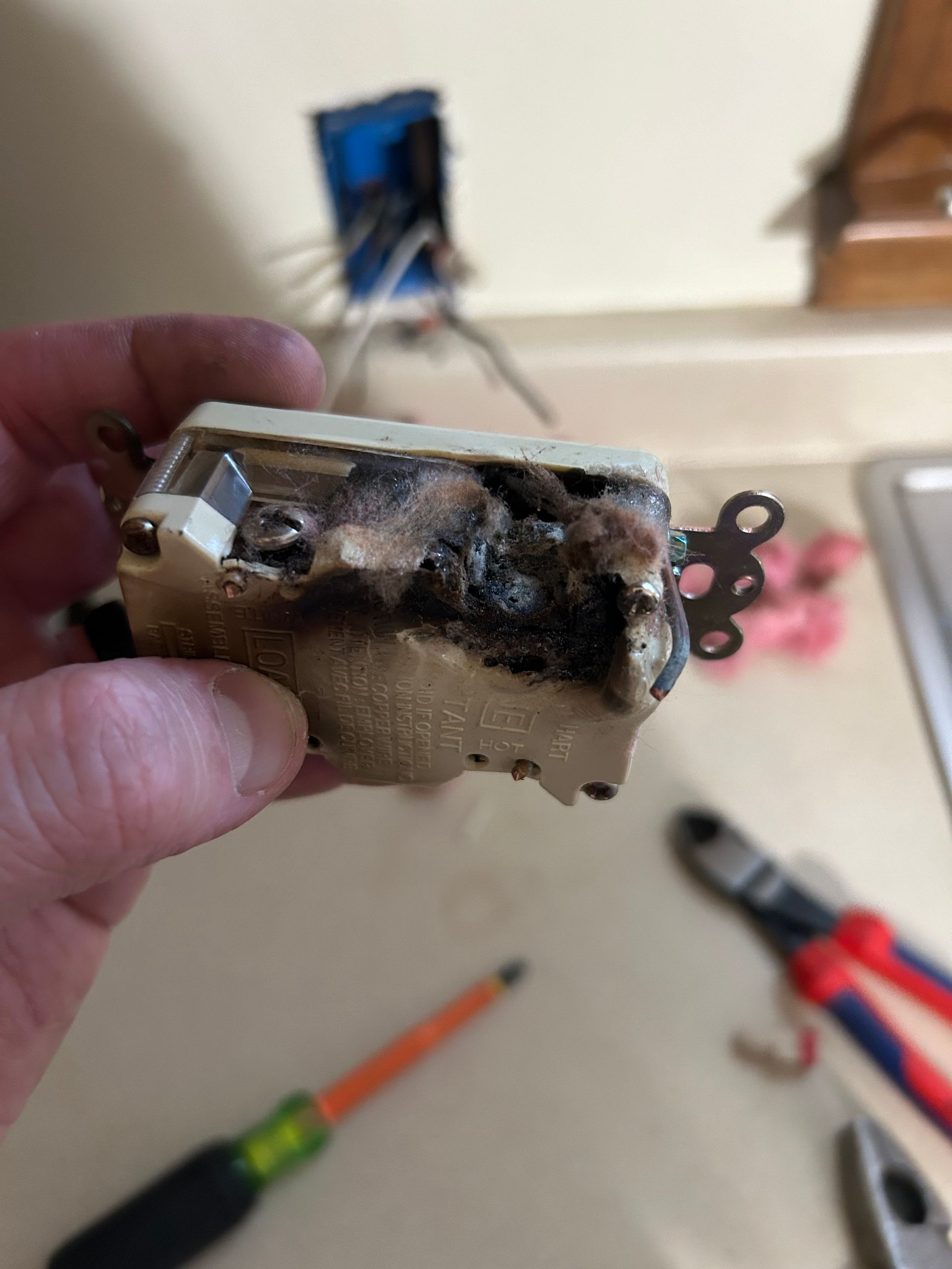 Close-up of a dirty electrical switch held in a hand, with tools blurred on the floor behind it.