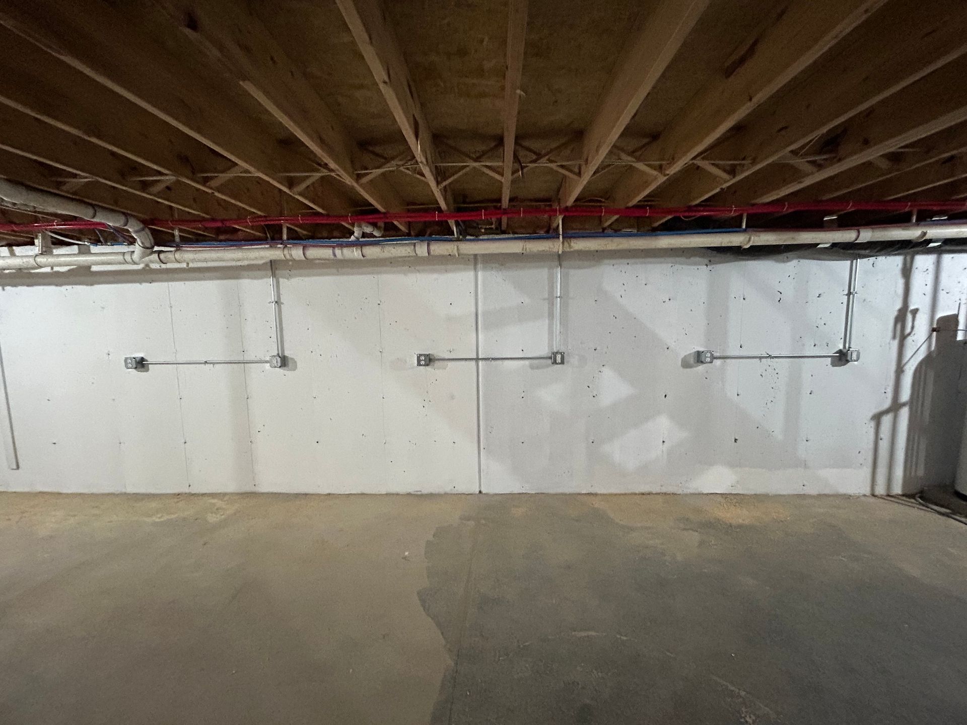 Empty unfinished basement with exposed wooden joists and white foundation walls.
