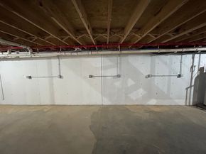 Empty basement with exposed joists, white foundation wall, and concrete floor