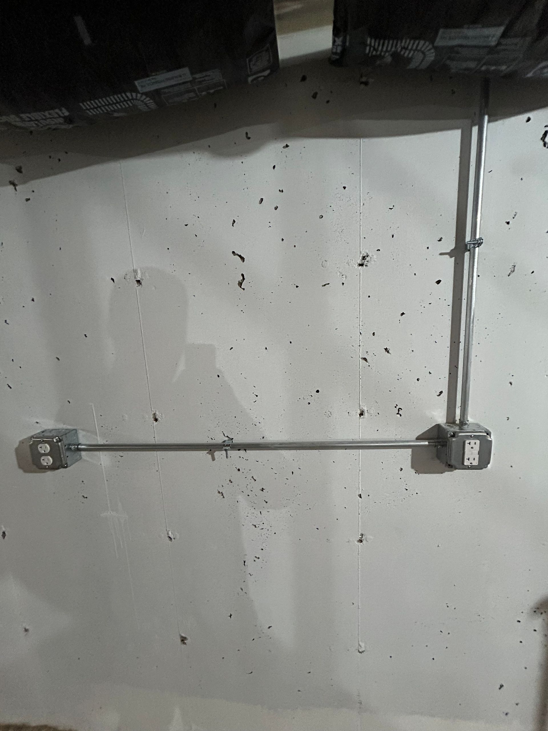 Metal conduit and cable mounted horizontally on a white wall in a dim utility space