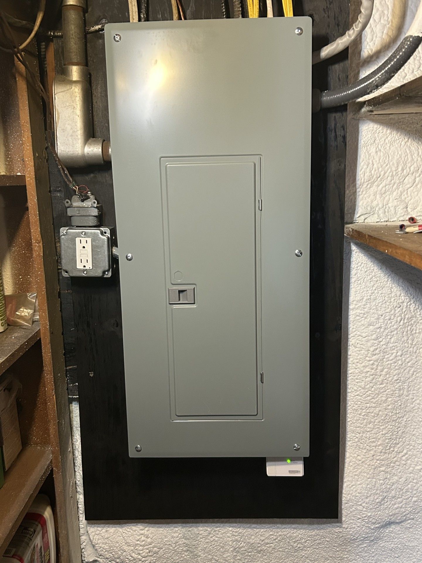 Gray electrical breaker panel mounted in a basement wall with wiring and conduit around it