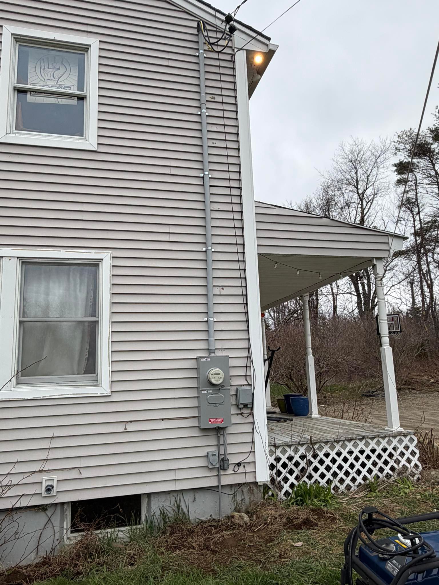 Side of a white house with utility meters, lit exterior light, and a small porch