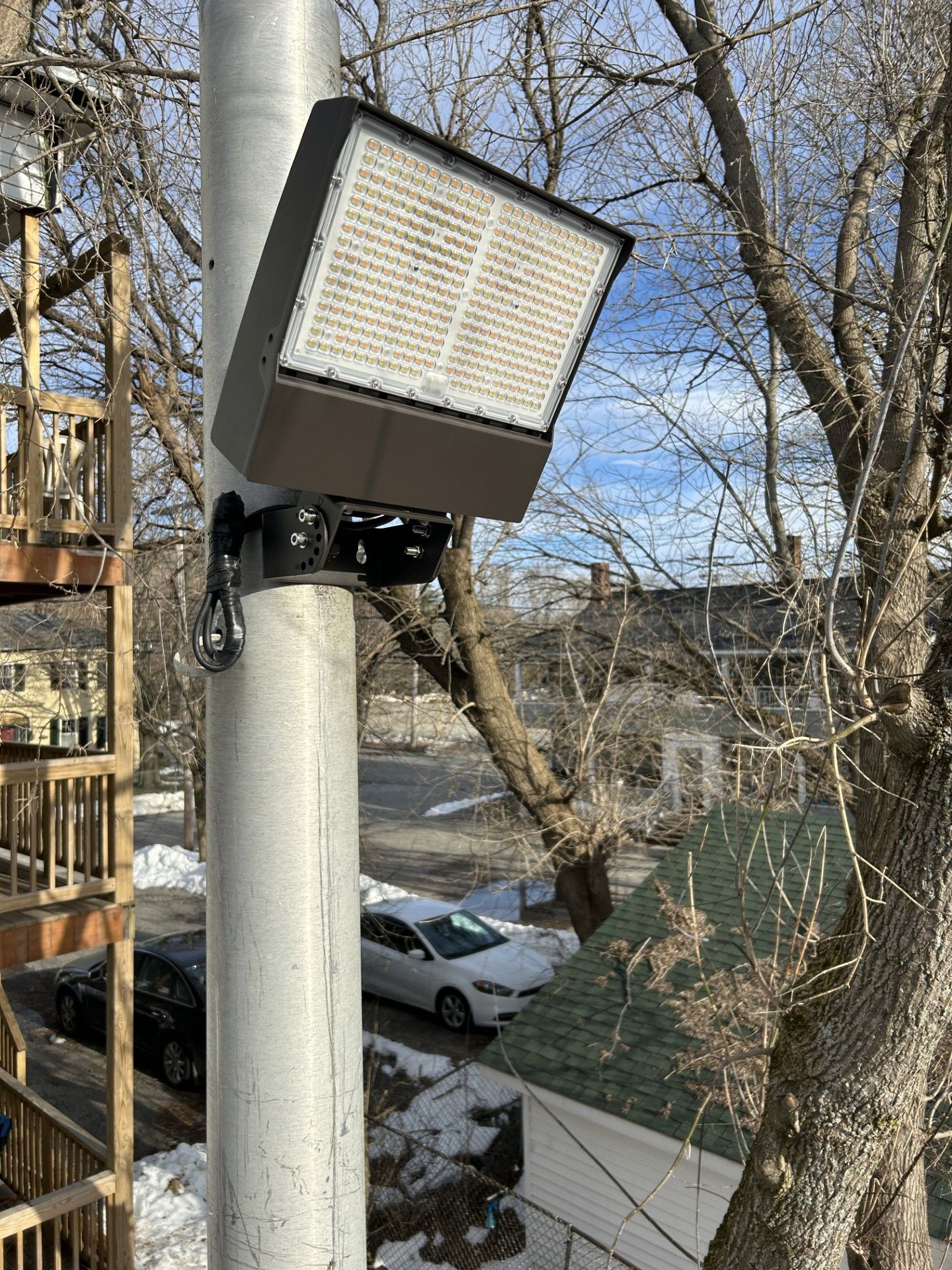 Square outdoor light on a pole beside trees and a sidewalk on a sunny day