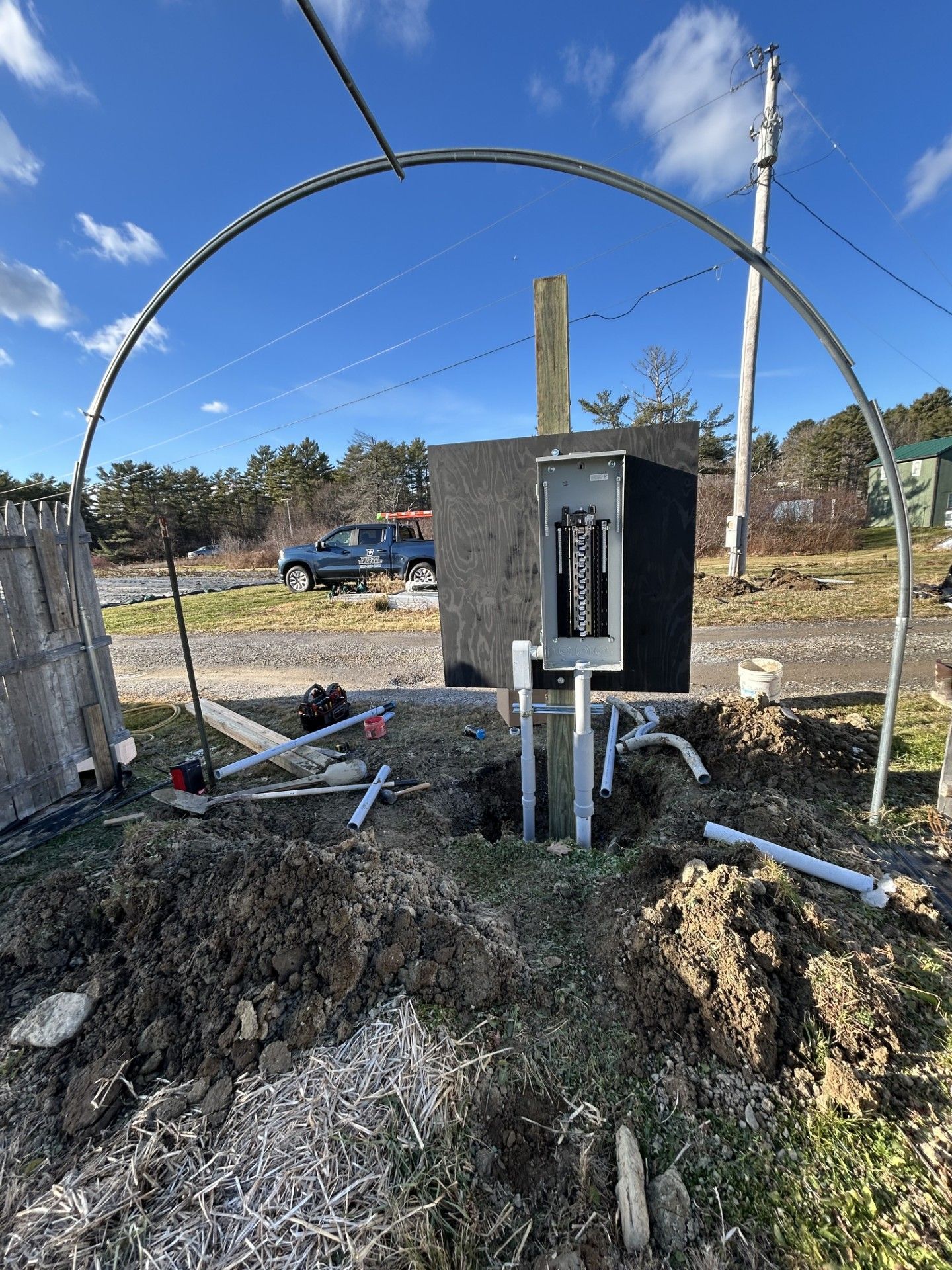 Electrical meter box and conduit setup beside a dirt trench under a large metal hoop outdoors.