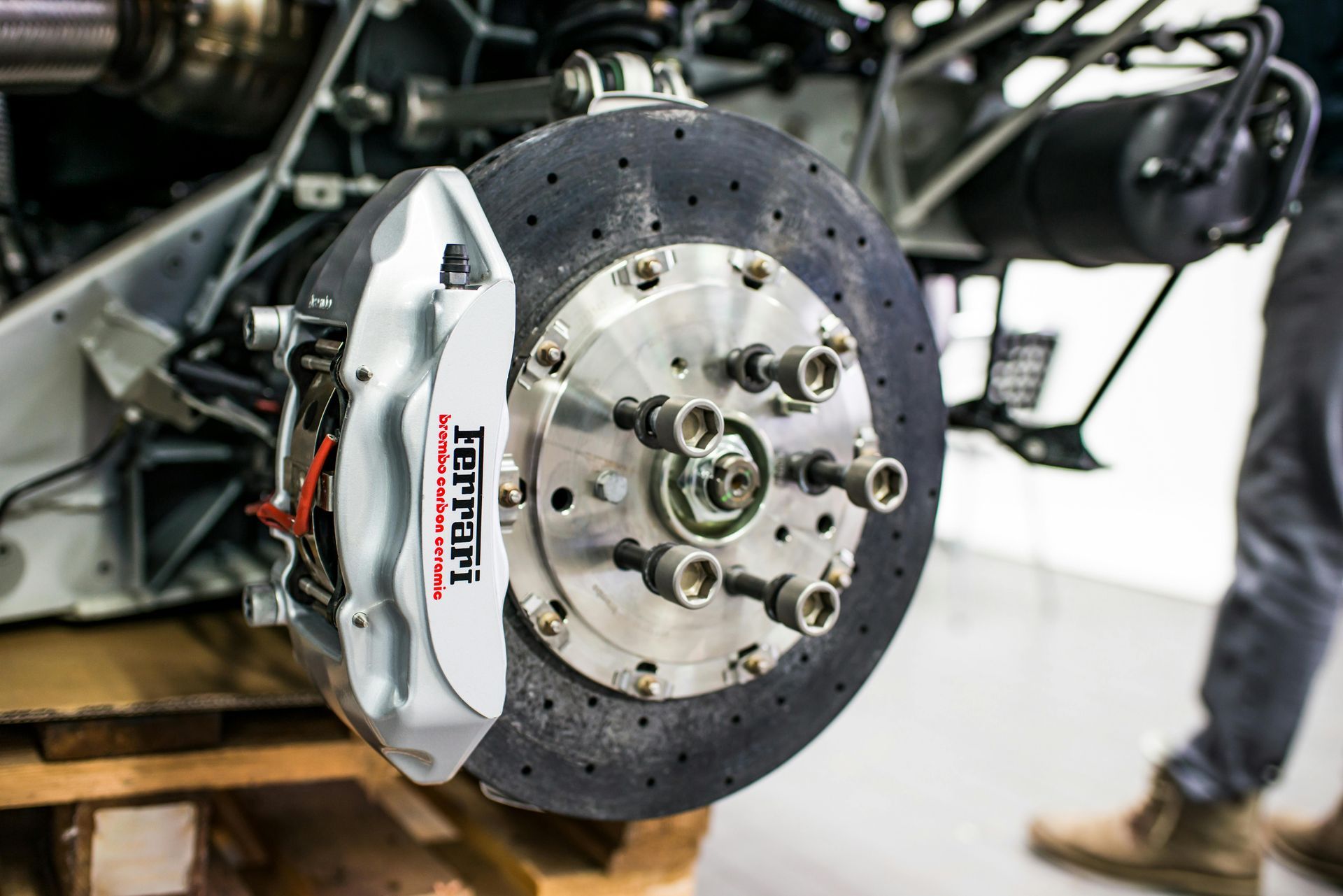A close-up of a Ferrari brake disc and caliper in silver and red, mounted on a wheel hub.