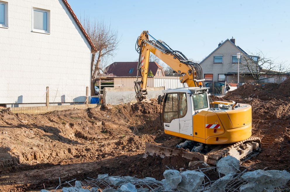 Yellow excavator digging a large dirt pit beside houses at a construction site