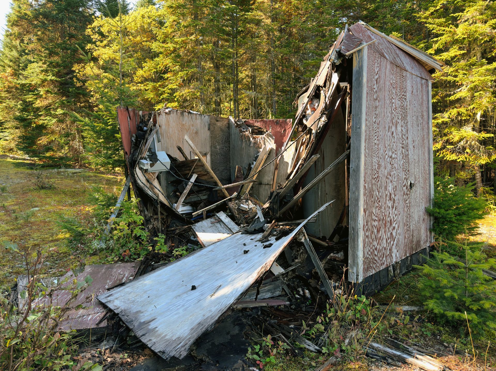 Collapsed wooden shed with broken roof and debris in a wooded yard