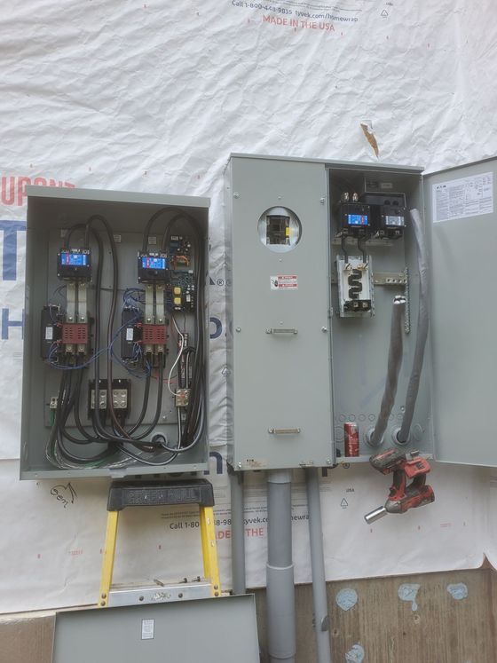 Electrical panel with open cover, exposing wiring and components, mounted on a building's exterior.