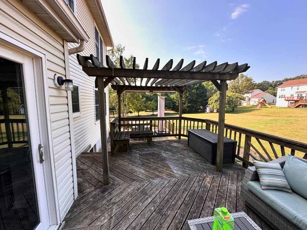 Wooden deck with pergola, bench, and outdoor furniture beside a house.