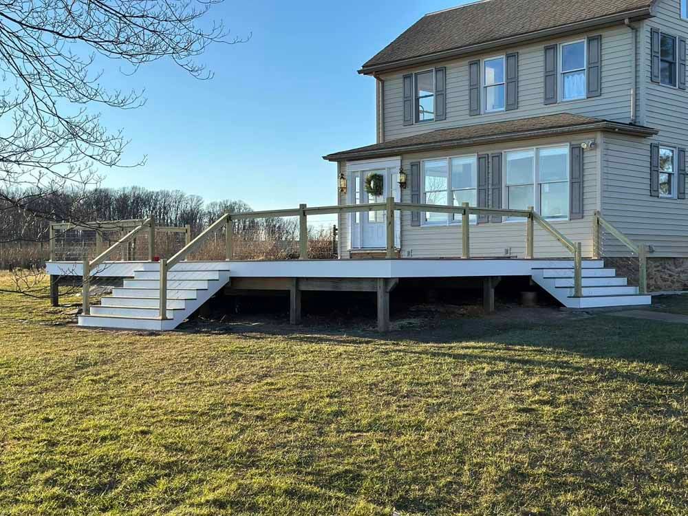 A two-story house with a wooden deck and steps, surrounded by grass under a blue sky.