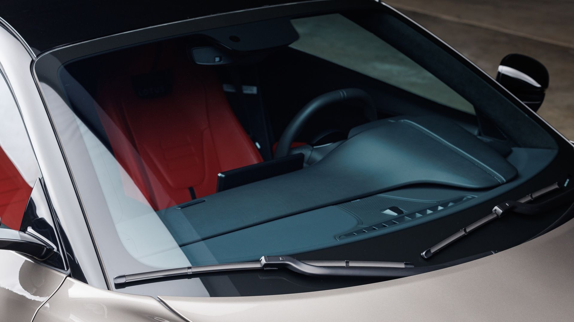 Close-up of a car windshield and hood, with a red interior visible inside.