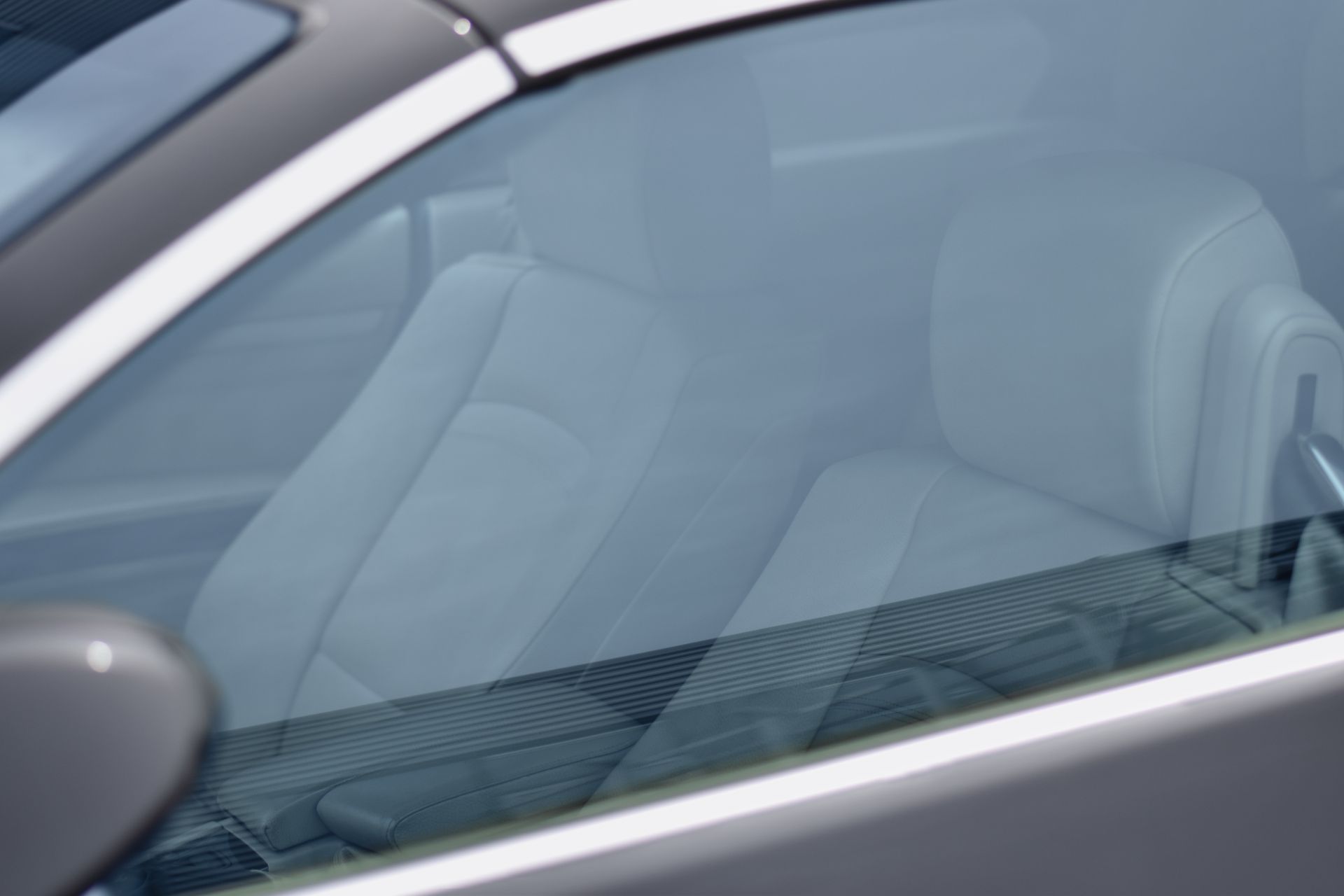 Car interior seen through a closed window, with a gray seat and dashboard visible