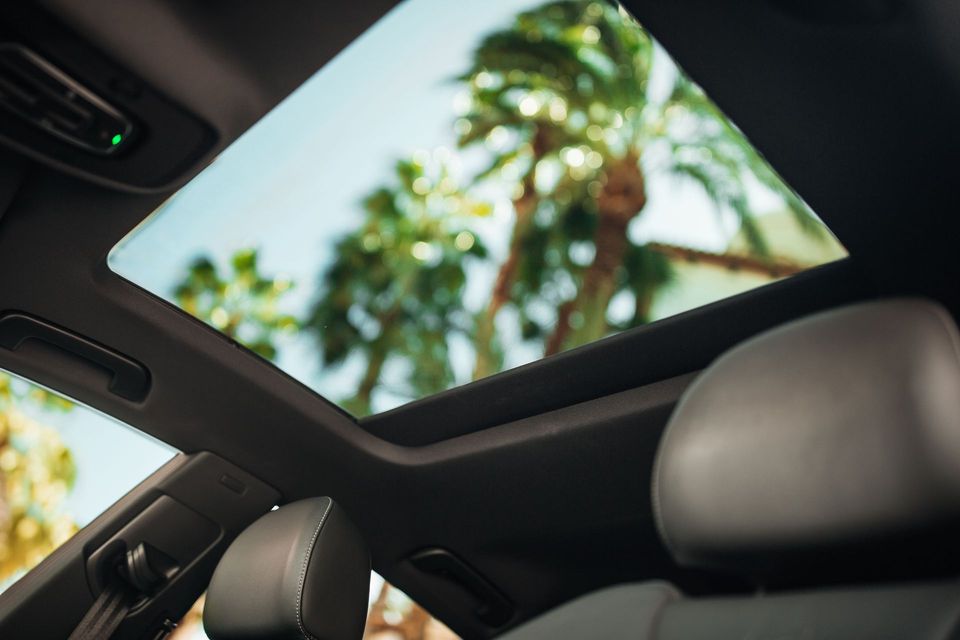 Car interior with open sunroof showing palm trees and blue sky overhead
