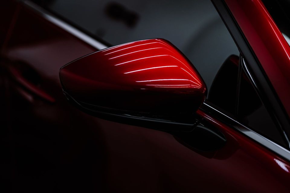 Close-up of a glossy red car side mirror on a dark vehicle