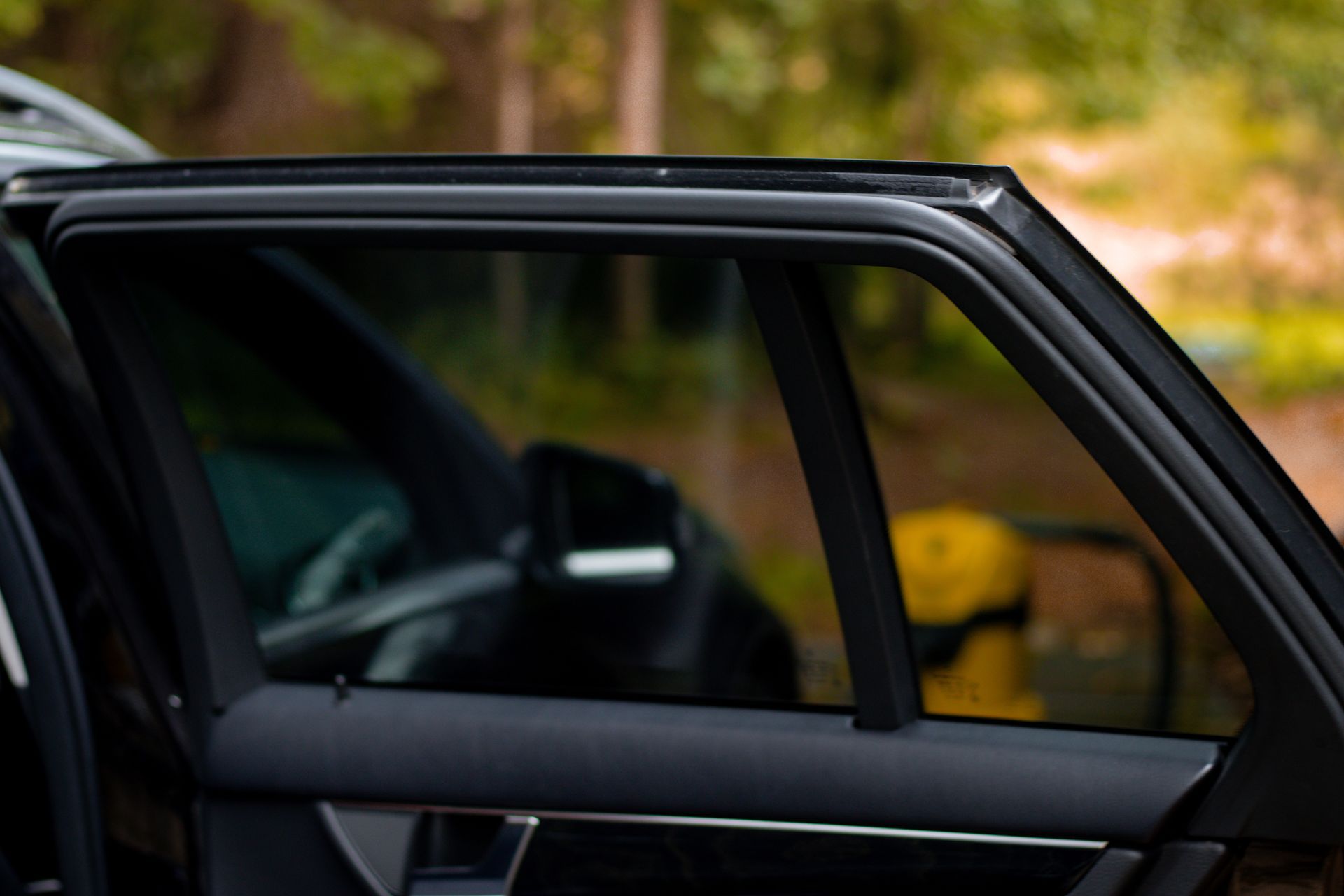 Open car rear door with dark interior, parked outdoors against a blurred autumn background