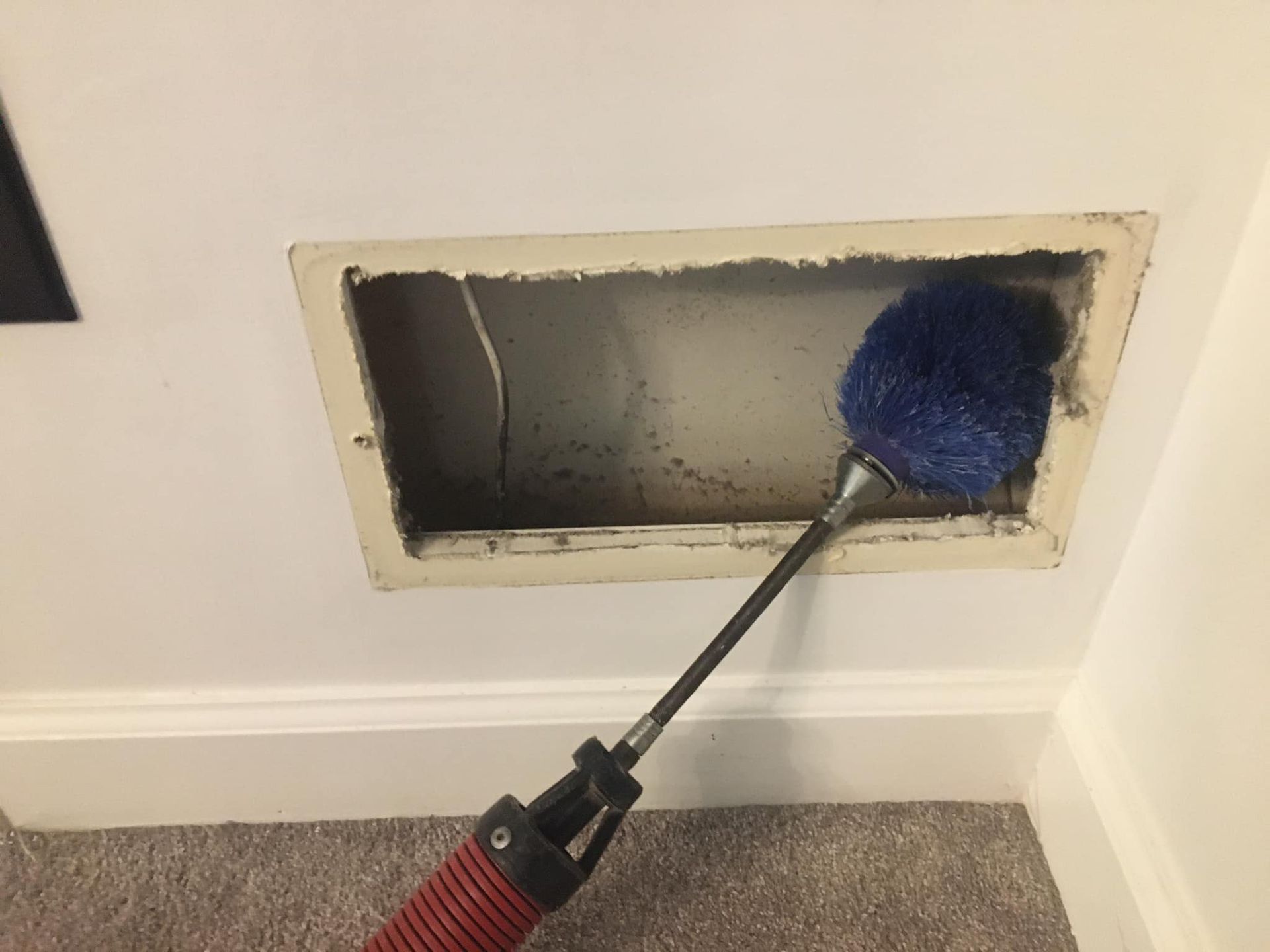A person is cleaning an air vent with a brush.