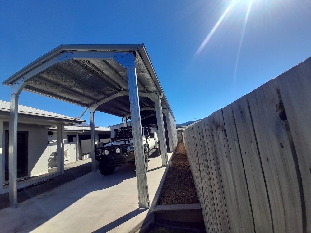 A Car Is Parked Under A Carport Next To A Wooden Fence — Whit Coast Sheds in Gregory River, QLD