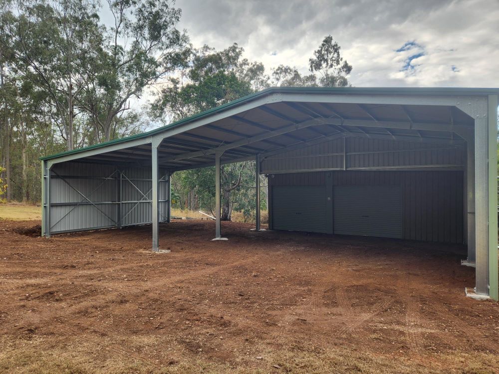 A Large Metal Building With A Green Roof Is Sitting In The Middle Of A Dirt Field — Whit Coast Sheds in  Gregory River, QLD