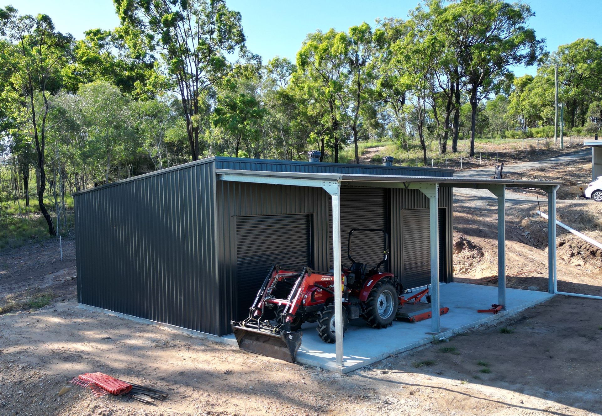 Dark Gray Metal Shed with an Open Side Carport Featuring a Red Tractor — Whit Coast Sheds in Gregory River, QLD
