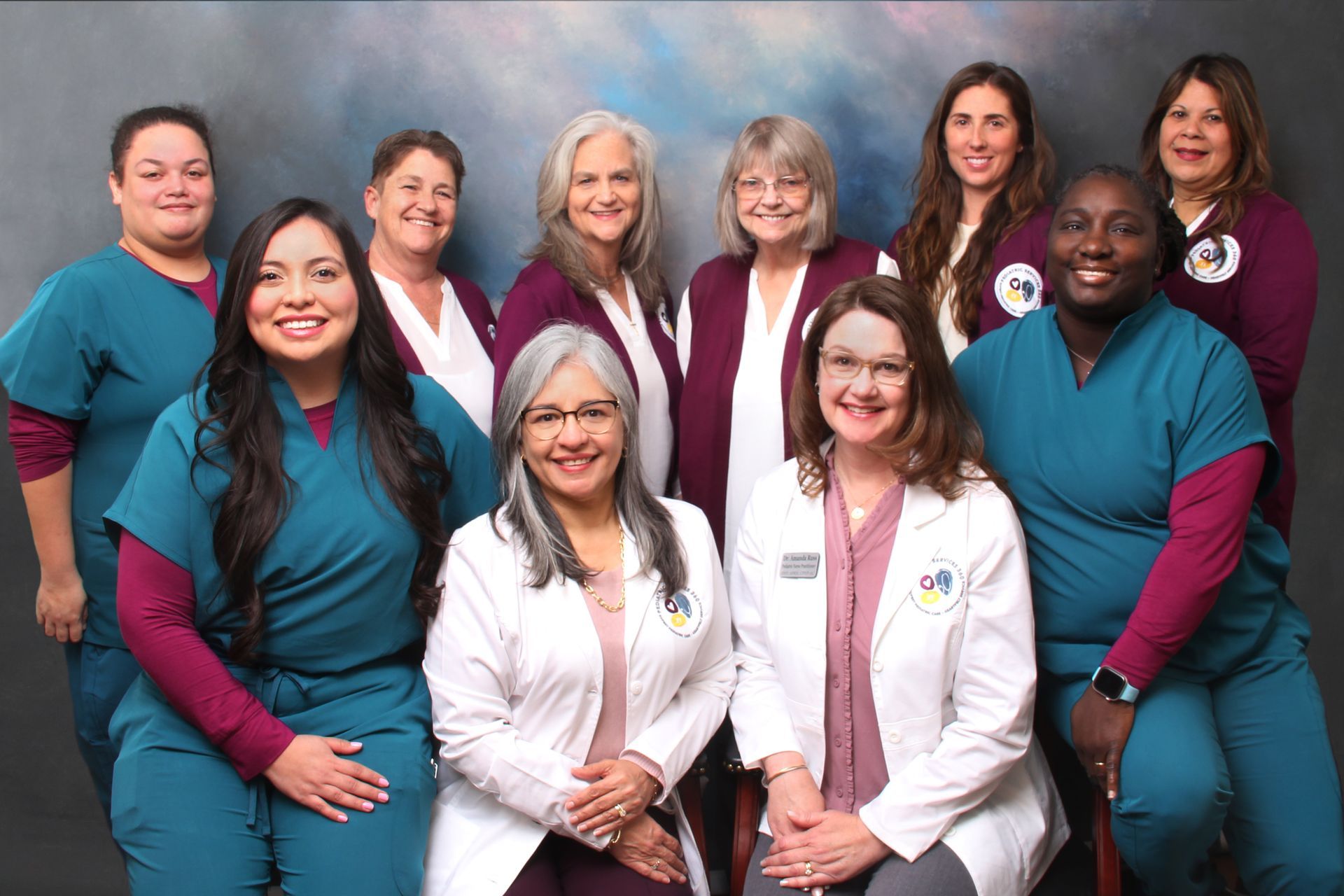 Group of healthcare professionals in teal scrubs and white coats, smiling.