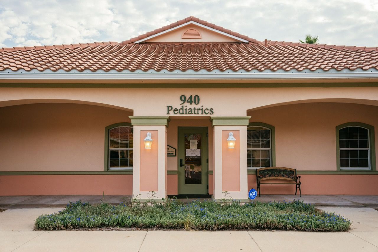 Exterior of a pediatric clinic at 940, light pink stucco with a clay tile roof. Green trim, windows, and entry door.