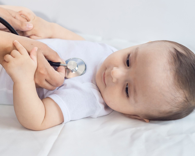 Baby lying down having their heart checked with a stethoscope.