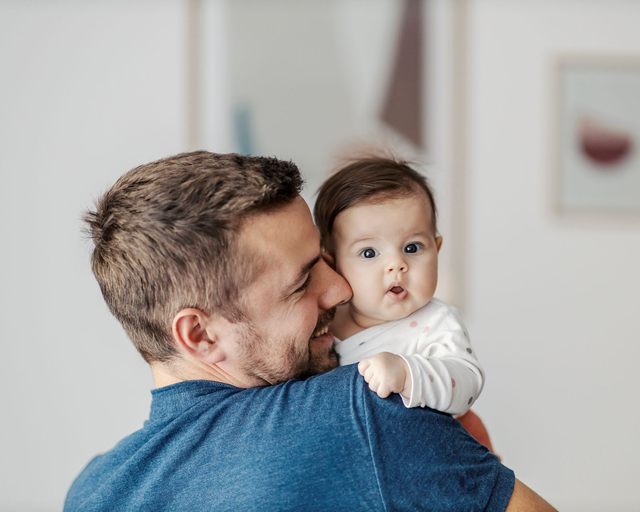 Man holding baby on his shoulder; both looking at viewer.