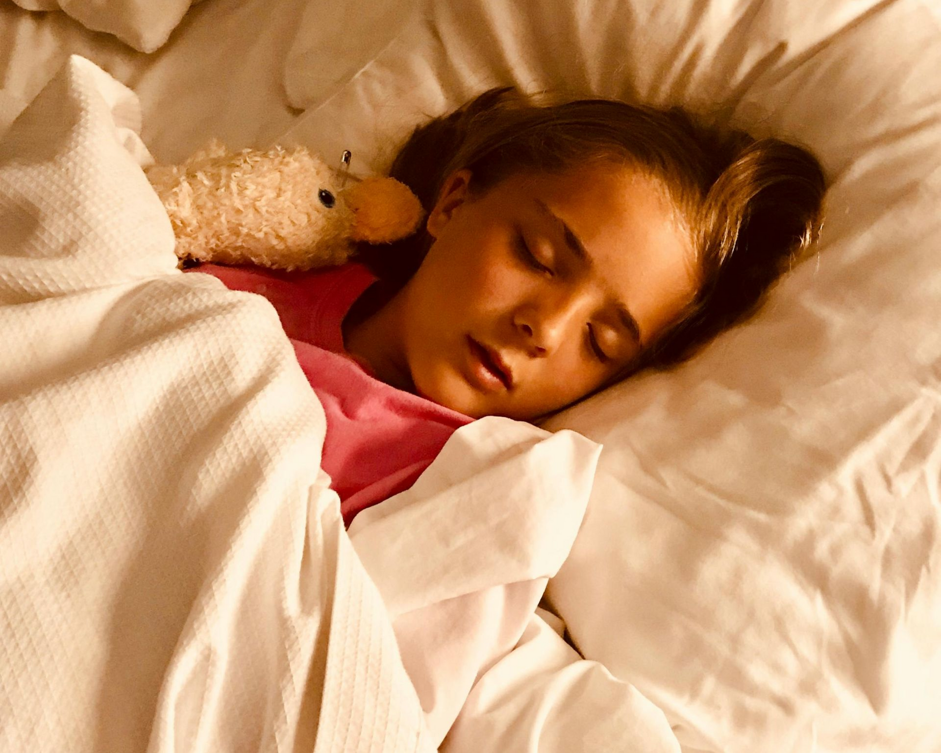 Girl sleeping in bed, cuddling a stuffed animal.