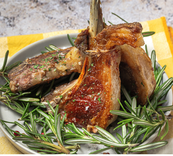 Grilled lamb chops garnished with rosemary on a white plate