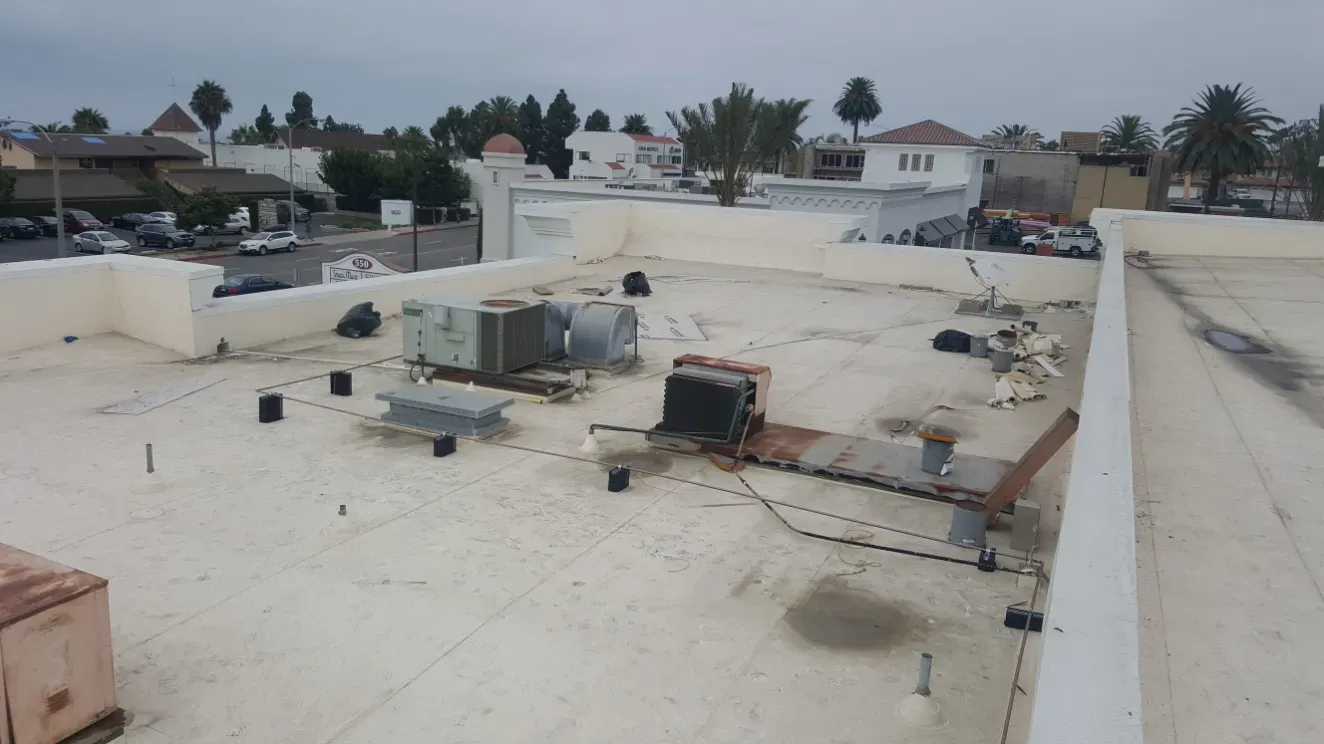 Flat rooftop with HVAC equipment and vents in a residential neighborhood under an overcast sky
