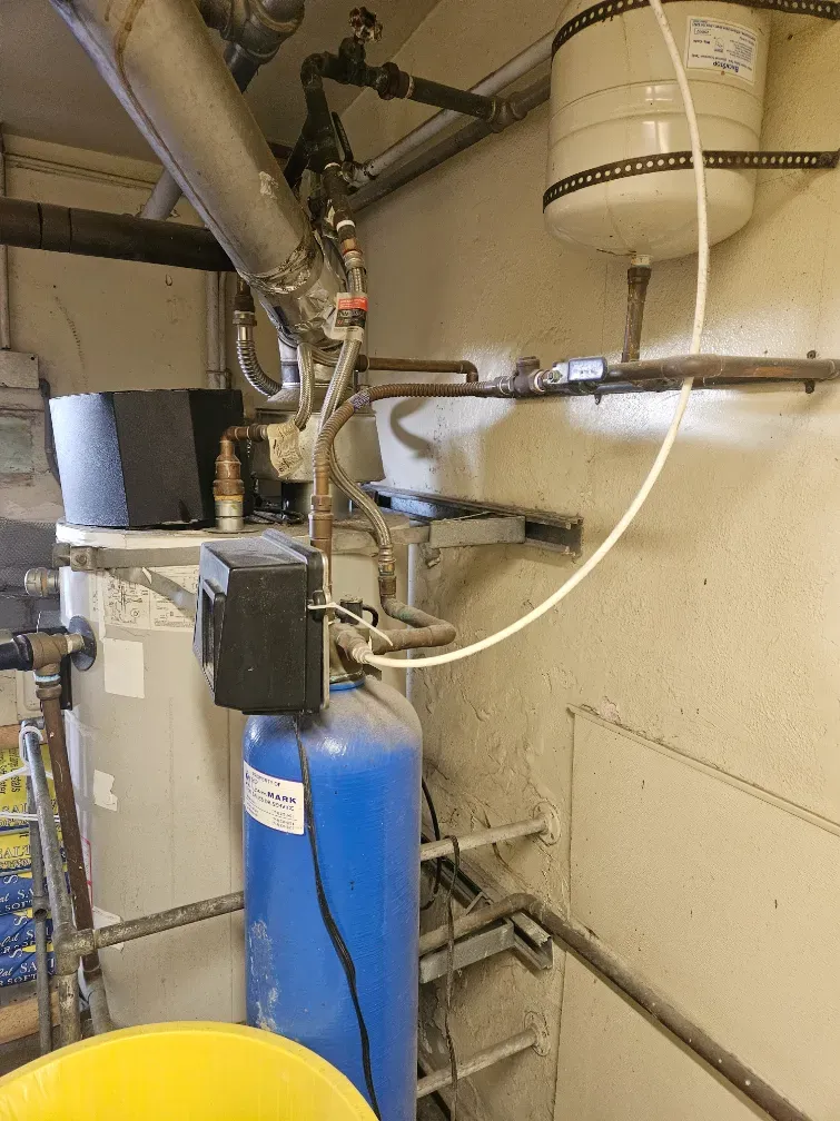 Basement plumbing with blue pressure tank, pipes, and white water heater on a beige wall
