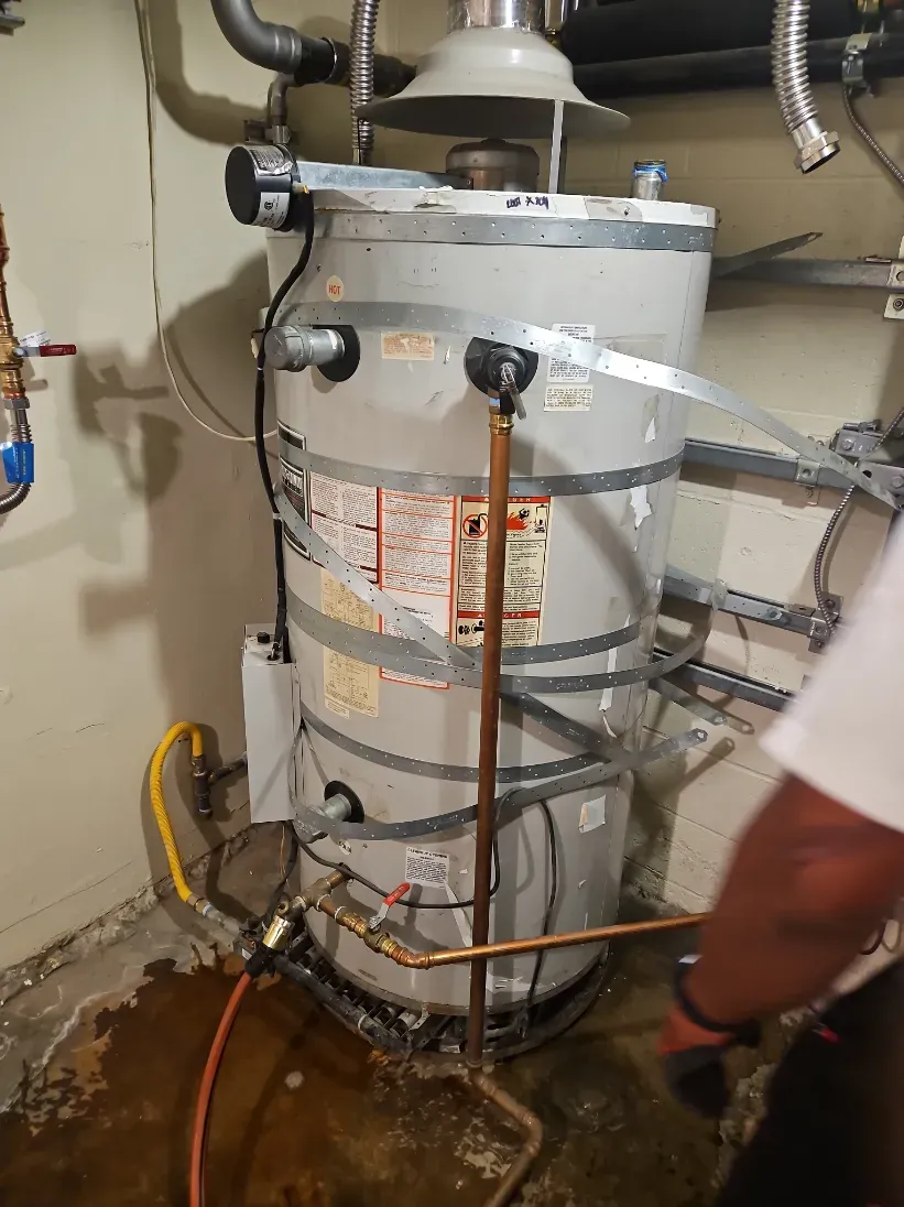 Water heater in a utility room with leaking water pooling on the floor and a person partially visible beside it