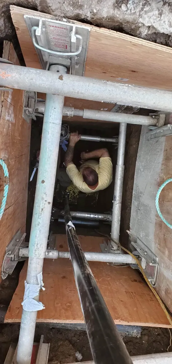 Looking down a ladder shaft into a narrow brick-lined well with pipes and a valve below