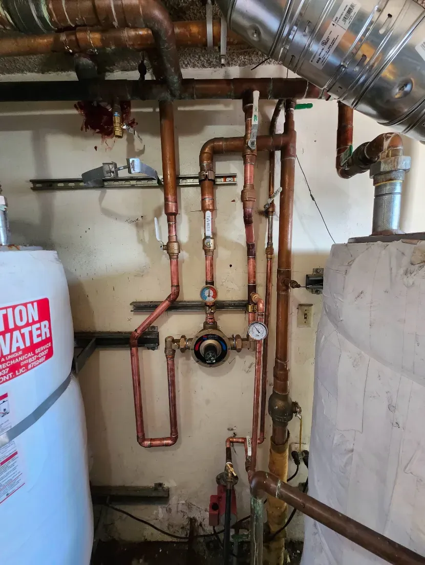Basement utility room with copper pipes, valves, water heater, and ductwork along the wall