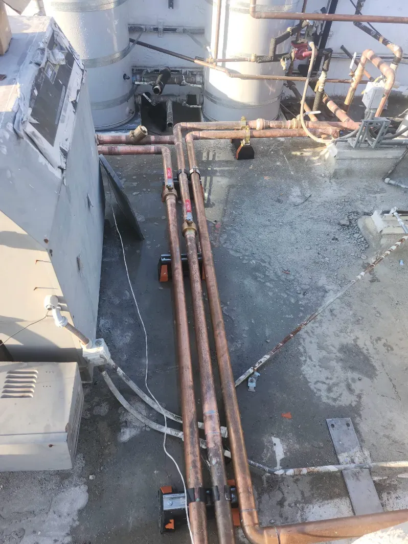 Rooftop utility pipes running along a weathered industrial surface beside large HVAC equipment