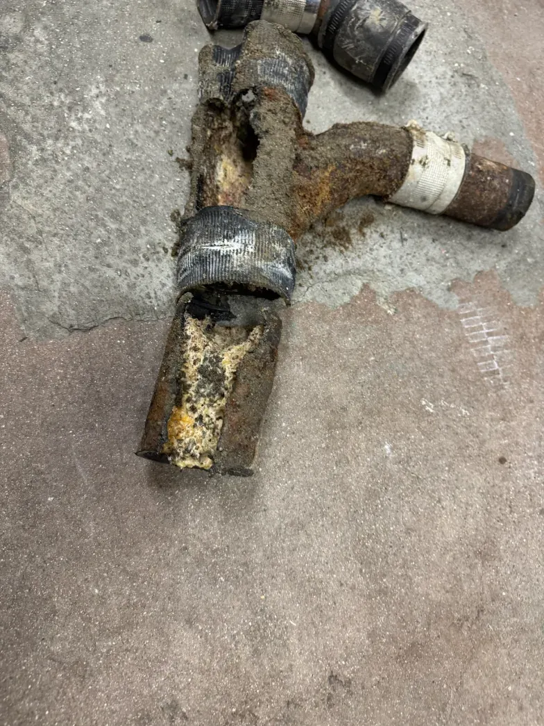 Corroded metal pipe junction with rust and taped sections on a concrete floor