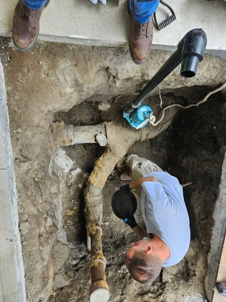 Worker inspecting a buried pipe in a trench beside a blue pump, viewed from above