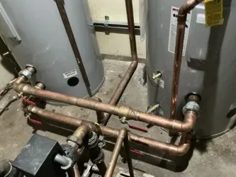 Copper plumbing manifold between two gray water heaters in a utility room