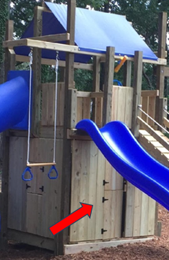 Wooden playground fort with blue slides; red arrow points to a lower gate latch.