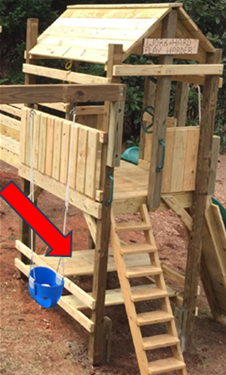 Wooden playhouse with stairs; red arrow points to a blue bucket attached near the base.