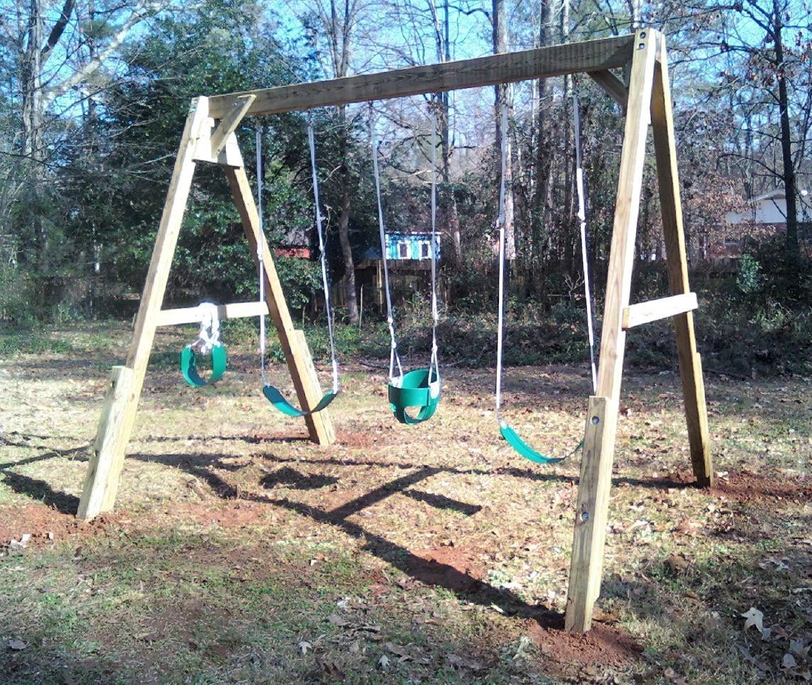 Wooden backyard swing set with four green swings on a sunny day