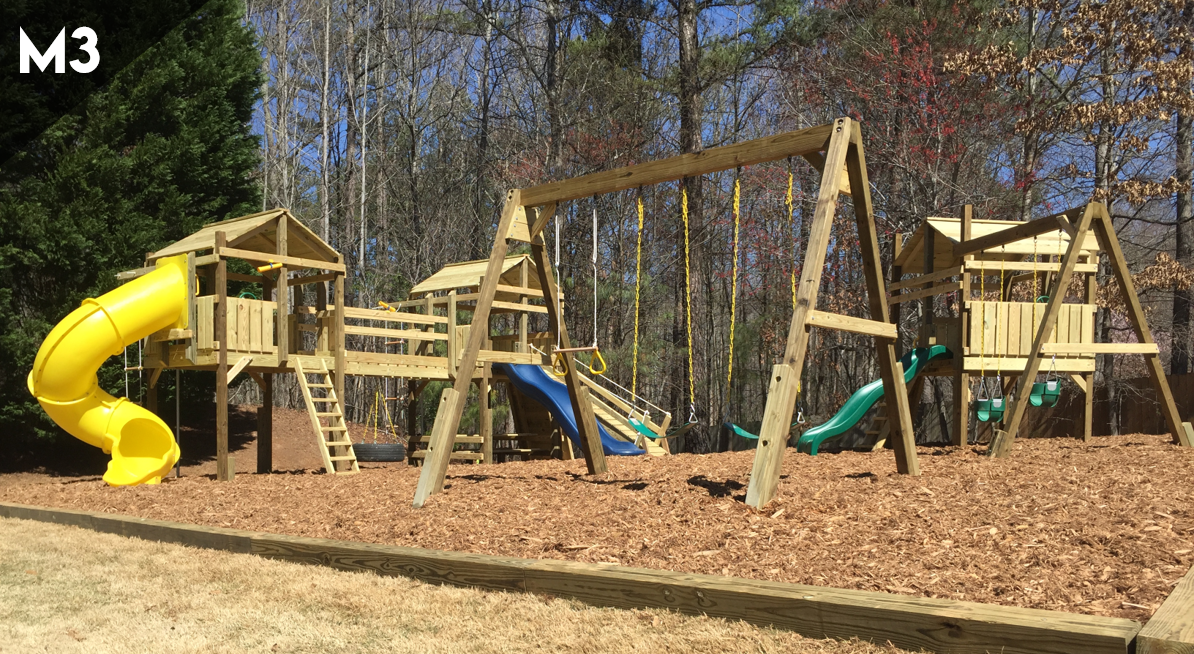 Outdoor wooden playground with yellow slide, swings, and climbing structures on a mulch-covered lot