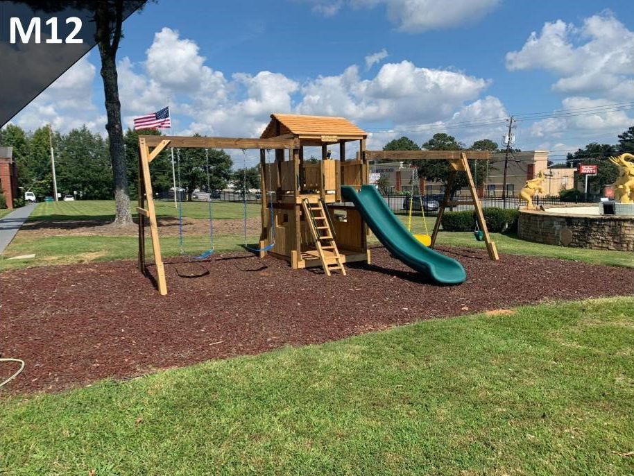 Playground with wooden climbing structure, green slide, and mulch under a sunny blue sky